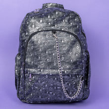 Load image into Gallery viewer, The Rustic Silver Spider Backpack sat on a purple background. The bag is facing forward to highlight the two zip front pockets, two elasticated side pockets, the double zip main compartment with a silver draping chain across the front. The vegan friendly faux leather bag has 3d embossed spiders in varying sizes with brushed black and silver tones all over.