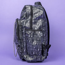 Load image into Gallery viewer, The Rustic Silver Spider Backpack sat on a purple background. The bag is facing left to highlight the two zip front pockets, two elasticated side pockets, the double zip main compartment with a silver draping chain across the front. The vegan friendly faux leather bag has 3d embossed spiders in varying sizes with brushed black and silver tones all over.