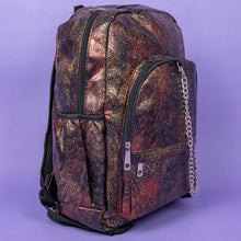 Load image into Gallery viewer, The Rustic Skulls & Roses Backpack sat on a purple background. The bag is facing forward angled right to highlight the two zip front pockets, two elasticated side pockets, the double zip main compartment with a silver draping chain across the front. The bag is varying colours of bronze, gold, rose and brown with black 3d embossed sugar skulls, roses and swirls all over.