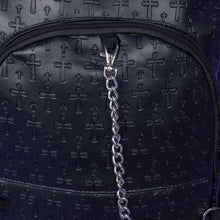 Load image into Gallery viewer, A close up of the Black Embossed Cross Backpack sat on a purple background. The backpack is facing forward to highlight the two front silver zip pockets, two elasticated side pockets, main double zip compartment and a silver decorative detachable silver chain draping across the front. The bag is made of vegan friendly leather with 3d embossed crosses in varying sizes all over.