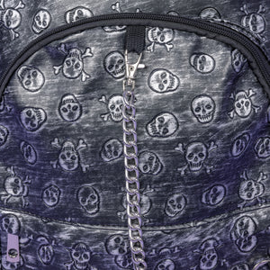 The Rustic Skulls Backpack sat on a purple background. A close up of the bag decorative silver chain detailing across the front. All over the backpack is an embossed 3d texture skulls and skull and crossbones on a faux leather material in a brushed black and silver grunge style.