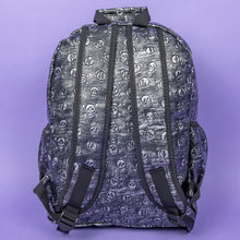 Load image into Gallery viewer, The Rustic Skulls Backpack sat on a purple background. The bag is facing away to highlight the two padded shoulder straps, two elasticated side pockets, main zip compartment and the top handle. All over the backpack is an embossed 3d texture skulls and skull and crossbones on a faux leather material in a brushed black and silver grunge style.