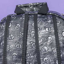 Load image into Gallery viewer, The Rustic Skulls Backpack sat on a purple background. A close up of the bag top handle and back padded shoulder straps. All over the backpack is an embossed 3d texture skulls and skull and crossbones on a faux leather material in a brushed black and silver grunge style.