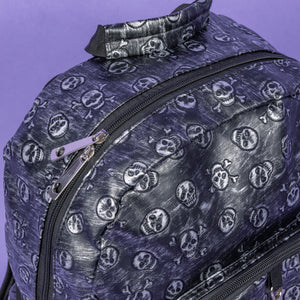 The Rustic Skulls Backpack sat on a purple background. A close up of the bag top handle and double zip opening main compartment. All over the backpack is an embossed 3d texture skulls and skull and crossbones on a faux leather material in a brushed black and silver grunge style.