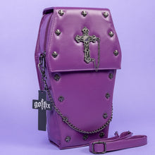 Load image into Gallery viewer, The GothX Purple Coffin Backpack. sat facing forward angled slightly right on a lilac background. The coffin bag in a sleek faux leather is a coffin shape with a magnetic close clip flap with a cross chain emblem in the centre, surrounding the coffin shape is mini metal cross studs. Draping across the front of a silver detachable decorative chain with the GothX black cross tag hanging to the left side.
