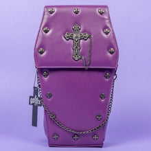 Load image into Gallery viewer, The GothX Purple Coffin Backpack. sat facing forward on a lilac background. The coffin bag in a sleek faux leather is a coffin shape with a magnetic close clip flap with a cross chain emblem in the centre, surrounding the coffin shape is mini metal cross studs. Draping across the front of a silver detachable decorative chain with the GothX black cross tag hanging to the left side.
