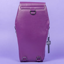 Load image into Gallery viewer, The GothX Purple Coffin Backpack is sat facing away on a lilac background. The coffin bag in a sleek faux leather is a coffin shape. On either side are D rings for the detachable and adjustable strap, there is also a D ring and two D rings at the top to rethread the strap through to make it a backpack with the GothX black cross tag hanging to the right side.
