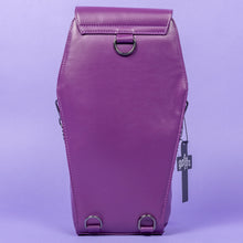 Load image into Gallery viewer, The GothX Purple Coffin Backpack is sat facing away on a lilac background. The coffin bag in a sleek faux leather is a coffin shape. On either side are D rings for the detachable and adjustable strap, there is also a D ring and two D rings at the top to rethread the strap through to make it a backpack with the GothX black cross tag hanging to the right side.