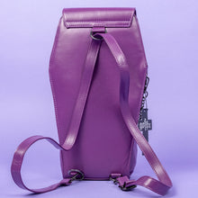 Load image into Gallery viewer, The GothX Purple Coffin Backpack is sat facing away on a lilac background. The coffin bag in a sleek faux leather is a coffin shape with a detachable adjustable strap threaded through the back. On either side are D rings for the detachable and adjustable strap, there is also a D ring and two D rings at the top to rethread the strap through to make it a backpack with the GothX black cross tag hanging to the right side.