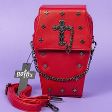 Load image into Gallery viewer, The GothX Red Mini Coffin Bag facing forward on a purple background. The coffin bag is made with vegan friendly sleek red leather and features a detachable decorative metal chain with a large metal cross and chain emblem with surrounding cross studs. The detachable adjustable strap is sat folded up in front of the mini bag.
