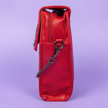 Load image into Gallery viewer, The GothX Red Mini Coffin Bag facing left to highlight the clip close magnetic flap and main zip compartment on a purple background. The coffin bag is made with vegan friendly sleek red leather and features a detachable decorative metal chain with a large metal cross and chain emblem with surrounding cross studs.