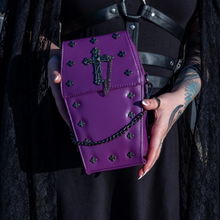 Load image into Gallery viewer, The GothX Purple Mini Coffin Bag being held up by a gothic model wearing a goth black dress with red hair. The coffin bag in a sleek faux leather is a coffin shape with a magnetic close clip flap with a cross chain emblem in the centre, surrounding the coffin shape is mini metal cross studs. Draping across the front of a silver detachable decorative chain with the GothX black cross tag hanging to the left side.