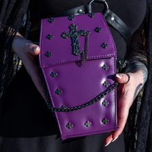 Load image into Gallery viewer, The GothX Purple Mini Coffin Bag being held up by a gothic model wearing a goth black dress with red hair. The coffin bag in a sleek faux leather is a coffin shape with a magnetic close clip flap with a cross chain emblem in the centre, surrounding the coffin shape is mini metal cross studs. Draping across the front of a silver detachable decorative chain with the GothX black cross tag hanging to the left side.