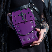 Load image into Gallery viewer, The GothX Purple Mini Coffin Bag being held up by a gothic model wearing a goth black dress with red hair. The coffin bag in a sleek faux leather is a coffin shape with a magnetic close clip flap with a cross chain emblem in the centre, surrounding the coffin shape is mini metal cross studs. Draping across the front of a silver detachable decorative chain with the GothX black cross tag hanging to the left side.