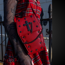 Load image into Gallery viewer, A goth model wearing an emo red tartan dress with the GothX Red Mini Coffin Bag on their shoulder. The coffin bag is made with vegan friendly sleek red leather and features a detachable decorative metal chain with metal cross studding.