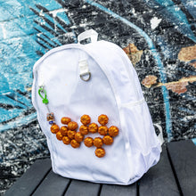 Load image into Gallery viewer, The White & Clear Window Ita Backpack sat on a wooden table in front of a graffiti wall. The bag is facing forward to highlight the clear front window filled with glittery pumpkins and two metal D rings with a keyring attached, two side elasticated pockets, main zip compartment and top handle. The vegan friendly bag is inspired by kawaii jfashion.