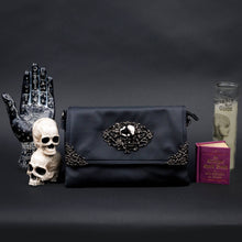 Load image into Gallery viewer, Black gothic crossbody bag by CHOK GothX styled in a gothic aesthetic display with a hand sculpture, spellbook, and vintage candle.