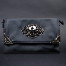 Load image into Gallery viewer, CHOK GothX black vegan leather clutch bag styled on a plain black background. The bag is facing forward to highlight the metal intricate skull centre emblem and metal floral corner detailing on the clip close flap.