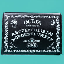Load image into Gallery viewer, The GothX Ouija Spirit Book Mini Bag sat on a teal background. The bag is forward to highlight the ouija spirit book white printed detailing on the black book bag with the 3D planchette stitching. Bag is inspired by witchy style and necromancy.