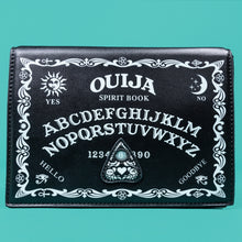 Load image into Gallery viewer, The GothX Ouija Spirit Book Mini Bag sat on a teal background. The bag is forward to highlight the ouija spirit book white printed detailing on the black book bag with the 3D planchette stitching. Bag is inspired by witchy style and necromancy.
