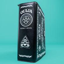 Load image into Gallery viewer, The GothX Ouija Spirit Book Mini Bag sat on a teal background. The bag is forward to highlight the ouija spirit book white printed detailing on the black book bag spine and front with the 3D planchette stitching. Bag is inspired by witchy style and necromancy.