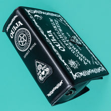 Load image into Gallery viewer, The GothX Ouija Spirit Book Mini Bag sat on a teal background. The bag is forward to highlight the ouija spirit book white printed detailing on the black book bag spine and front with the 3D planchette stitching. Bag is inspired by witchy style and necromancy.
