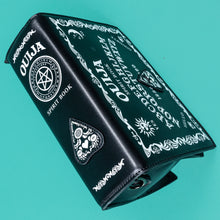 Load image into Gallery viewer, The GothX Ouija Spirit Book Mini Bag sat on a teal background. The bag is forward to highlight the ouija spirit book white printed detailing on the black book bag spine and front with the 3D planchette stitching. Bag is inspired by witchy style and necromancy.