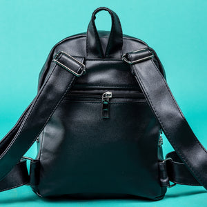A close up of the GothX black cross vegan stud mini backpack on a teal background. The vegan leather bag is facing away from camera to highlight the plain black back of the mini bag, the top handle, the adjustable shoulder straps and the hidden silver zip mini pocket.
