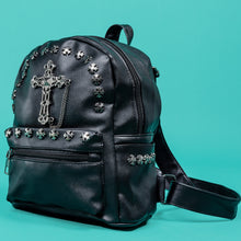 Load image into Gallery viewer, The GothX black cross vegan stud mini backpack on a teal background. The vegan leather bag is facing forward angled left to highlight the cross studs along the top zip line and top of zipped pocket, studded cross with chain centrepiece and side metal cross studs on the slot pockets.
