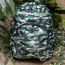 Load image into Gallery viewer, Classic Camouflage vegan backpack with chain sat outside in front of a tropical plant and brick wall. The backpack with a green and brown camo print is facing forward highlighting the two front zip pockets, two side pockets and silver decorative chain.