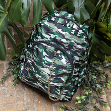 Load image into Gallery viewer, Classic Camouflage vegan backpack with chain sat outside in front of a tropical plant and brick wall. The backpack with a green and brown camo print is facing forward highlighting the two front zip pockets, two side pockets and silver decorative chain.