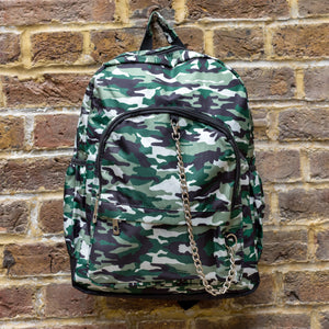 Classic Camouflage vegan backpack with chain hanging on a brick wall. The backpack with a green and brown camo print is facing forward highlighting the two front zip pockets, two side pockets and silver decorative chain.