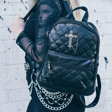 Load image into Gallery viewer, The GothX Quilted Cross Vegan Mini Backpack on the shoulder of a model wearing a black mesh top and black skirt. The mini bag has adjustable straps, quilted front and gunmetal coloured metal detailing with a cross appliqué.