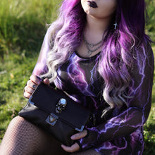 Load image into Gallery viewer, Model wearing a goth black and purple outfit holding the gothx crystal skull vegan shoulder bag on a grass field.