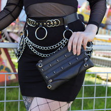 Load image into Gallery viewer, The gothx mini skull head vegan clutch bag being held by a model wearing a goth inspired outfit. The clutch is facing forward to highlight the skull studded front and faux zip detailing.
