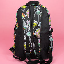 Load image into Gallery viewer, The kawaii graffiti doodle vegan backpack sat on a pink studio background. The bag is facing away to highlight the padded adjustable shoulder straps and the plain black back. The all over print has lollipops, pugs, rainbows, pizzas, polaroid cameras, eyes and fries.