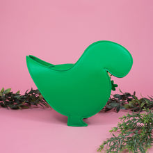 Load image into Gallery viewer, The kawaii green glitter dino vegan bag on a pink studio background with green foliage. The bag is facing away from camera to highlight the detachable strap and plain green back.