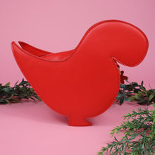 Load image into Gallery viewer, The kawaii red glitter dino vegan bag on a pink studio background with green foliage. The vegan leather red sparkly bag is facing away from camera to highlight the detachable strap and plain red back.