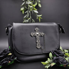 Load image into Gallery viewer, The gothx don&#39;t cross me vegan shoulder bag on a black studio background with green foliage and black roses surrounding it. The bag is facing forward to highlight the studded cross chain centrepiece.

