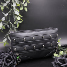 Load image into Gallery viewer, The gothx mini skull head vegan clutch bag on a black studio background with black roses and green leaf foliage surrounding it. The clutch is facing forward to highlight the skull studded front and faux zip detailing.