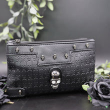 Load image into Gallery viewer, The gothx crystal skull vegan clutch bag on a black studio background with black roses and green foliage surrounding it. The bag is facing forward to highlight the embossed skull vegan black leather, mini skull studs, two main zip compartments and crystal skull centrepiece.