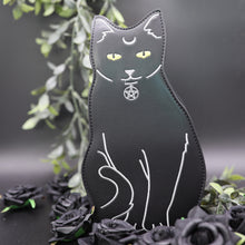 Load image into Gallery viewer, The gothx pagan black cat vegan shoulder bag on a black studio background with green foliage and black roses surrounding it. The bag is facing forward to highlight the embroidery details including a pentagram collar, yellow eyes and paws.
