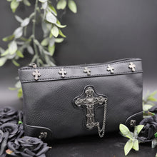 Load image into Gallery viewer, The gothx don't cross me vegan clutch bag on a black studio background with black roses and green foliage surrounding it. The clutch is facing forward to highlight the cross studs and stud, chain cross centrepiece.