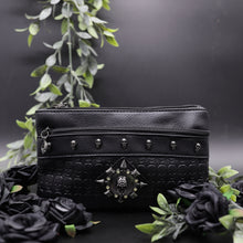 Load image into Gallery viewer, The gothx black skull vegan clutch bag on a black studio background with black roses and green foliage surrounding it. The clutch is facing forward to highlight the skull embossed vegan black leather, the crystal stud skull centrepiece, zip pocket and skull studs.
