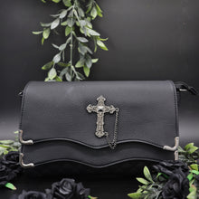 Load image into Gallery viewer, The GothX don't cross me quilted vegan clutch bag on a black studio background with black roses and green foliage surrounding it. The bag is facing forward to highlight the double quilted magnetic close clip flap with metal corners, quilted under layer and stud cross centrepiece with chain.