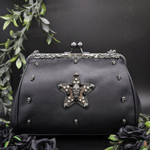 Load image into Gallery viewer, The GothX Skull-Struck vegan vintage clasp handbag on a black background with black roses and foliage surrounding it. The bag is facing forward to highlight the vintage ball clasp close, floral metal top detailing, detachable handle strap, skull studs and skull star with chains, studs and crystals.
