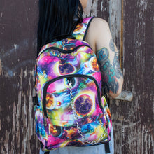 Load image into Gallery viewer, Model is standing in front of a painted brown wall wearing the pink and purple space galaxy vegan backpack. The backpack is facing forward to highlight the multicoloured space/planet/galaxy print, two zip pockets, two elastic side pockets and detachable silver chain.
