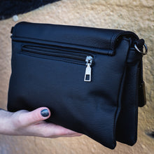 Load image into Gallery viewer, The GothX don't cross me vegan oversized clutch bag being held in front of a graffiti wall. Bag is facing away angled to the left to highlight the back zip pocket and detachable strap loops.