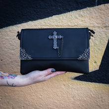 Load image into Gallery viewer, The GothX Don&#39;t cross me vegan oversized clutch bag being held in front of a graffiti wall. Bag is facing forward to highlight the metal lace effect detailing on the front flap corners and the studded cross with chain applique.
