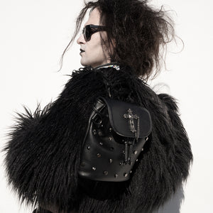 Model wearing a large black fluffy coat and sunglasses holding the goth dont cross me vegan tassel tie backpack on one shoulder. The bag is facing the camera to show the cross, skull & hexagon studs, tassel tie close and the cross chain emblem magnetic clip close flap.